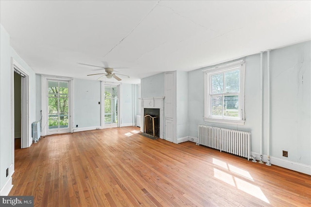 unfurnished living room with radiator heating unit, a ceiling fan, light wood finished floors, and a fireplace with flush hearth