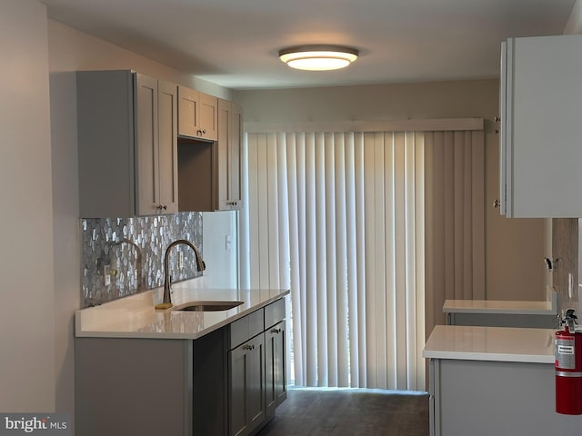 kitchen with a sink, gray cabinets, backsplash, and light countertops