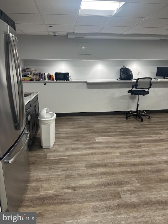 kitchen with wood finished floors, freestanding refrigerator, light countertops, and a drop ceiling