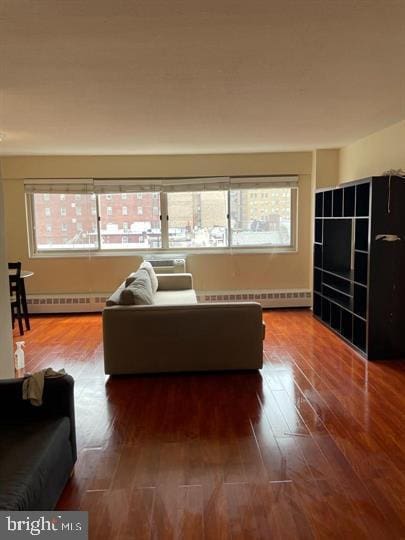 living room featuring dark wood-style flooring, an AC wall unit, plenty of natural light, and baseboard heating