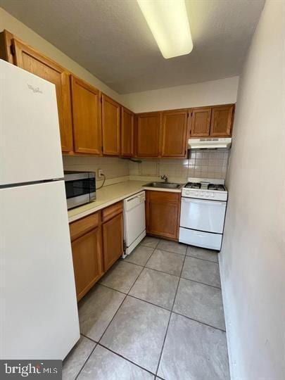 kitchen featuring tasteful backsplash, a sink, light countertops, white appliances, and under cabinet range hood