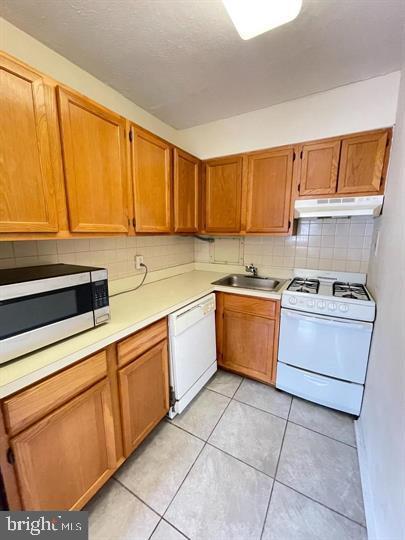 kitchen featuring tasteful backsplash, a sink, light countertops, white appliances, and under cabinet range hood