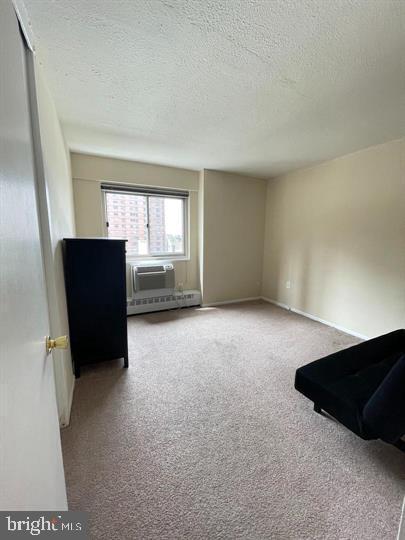 interior space featuring a wall mounted air conditioner, a textured ceiling, light carpet, and baseboard heating