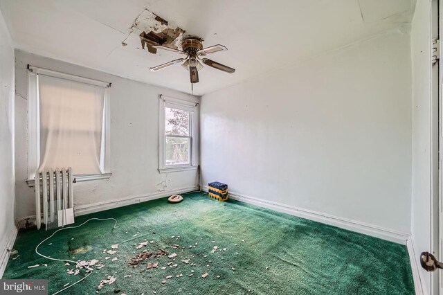 empty room with carpet floors, a ceiling fan, baseboards, and radiator heating unit