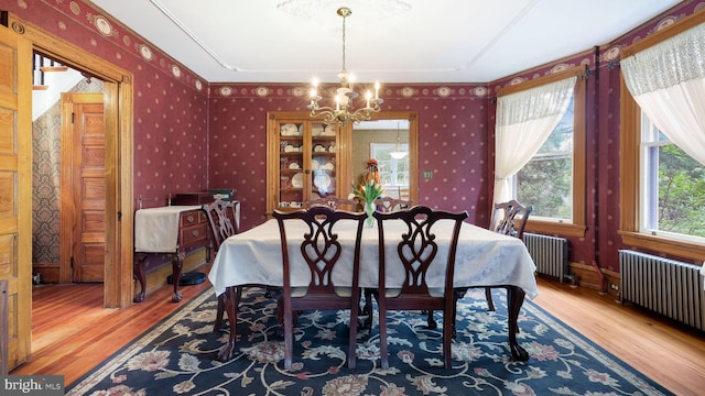 dining space featuring wallpapered walls, radiator heating unit, wood finished floors, and a notable chandelier
