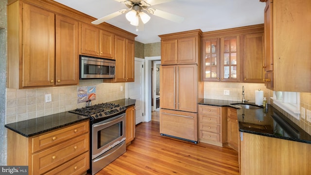 kitchen with a sink, dark stone counters, light wood-style flooring, tasteful backsplash, and appliances with stainless steel finishes