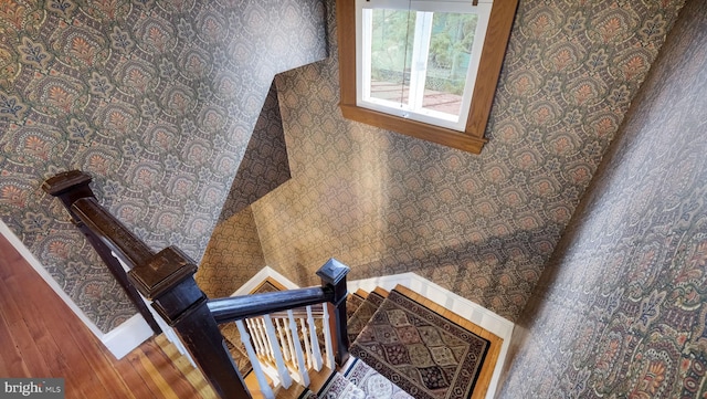 stairway featuring wood finished floors and wallpapered walls