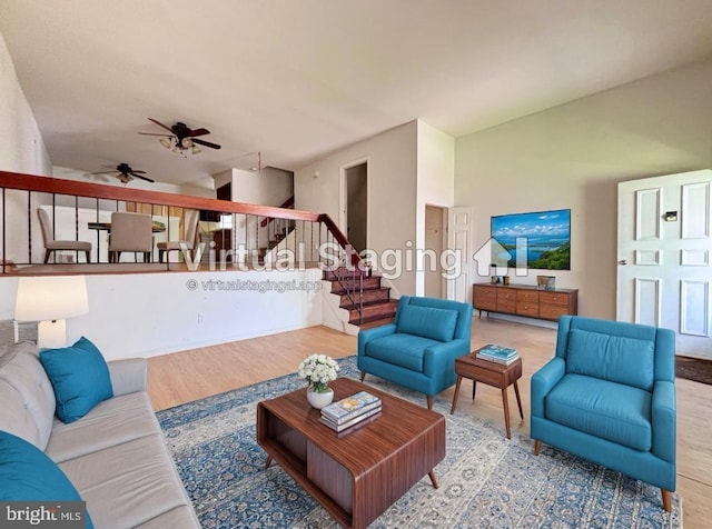 living area with ceiling fan, vaulted ceiling, wood finished floors, and stairway