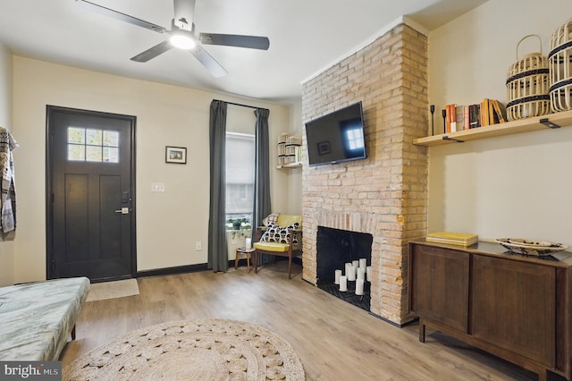 foyer featuring ceiling fan, light wood-type flooring, baseboards, and a brick fireplace