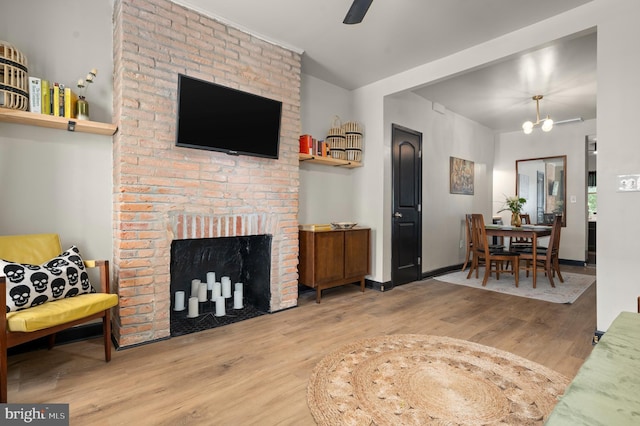 living area featuring wood finished floors, baseboards, and a brick fireplace
