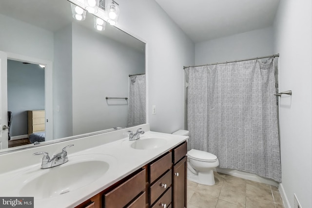 ensuite bathroom featuring toilet, double vanity, a sink, and tile patterned flooring