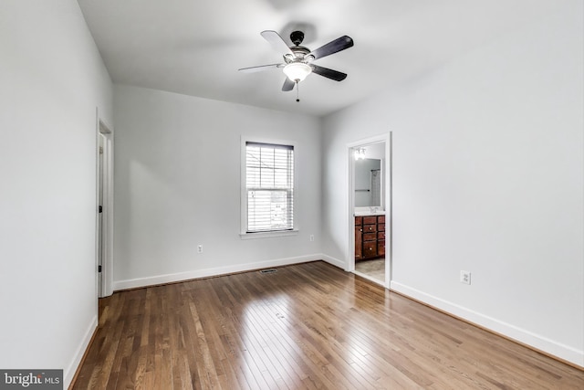 unfurnished bedroom featuring ensuite bathroom, a ceiling fan, visible vents, hardwood / wood-style floors, and baseboards