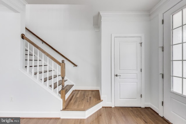stairway with wood finished floors, baseboards, and ornamental molding