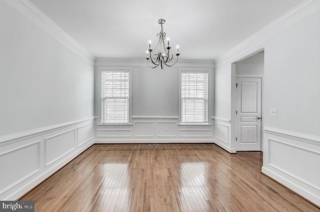 unfurnished dining area with an inviting chandelier, a decorative wall, ornamental molding, wainscoting, and hardwood / wood-style floors