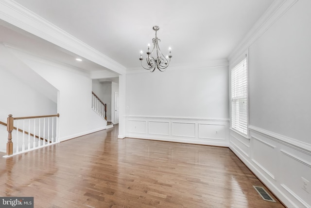 unfurnished dining area featuring visible vents, an inviting chandelier, crown molding, wood finished floors, and a wainscoted wall