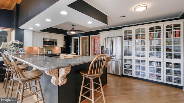 kitchen with a peninsula, white cabinets, visible vents, stainless steel appliances, and a sink
