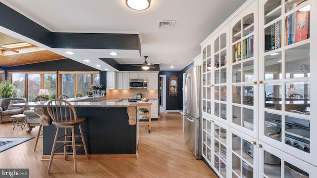 kitchen featuring stone counters, a kitchen breakfast bar, white cabinets, visible vents, and appliances with stainless steel finishes