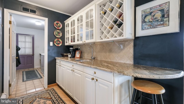 kitchen featuring tasteful backsplash, glass insert cabinets, white cabinetry, visible vents, and a sink