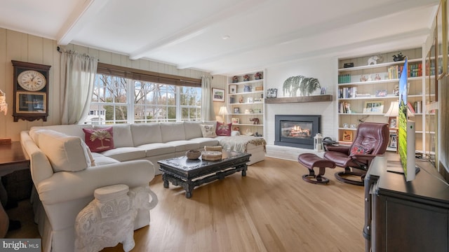 living area with a brick fireplace, beamed ceiling, and wood finished floors