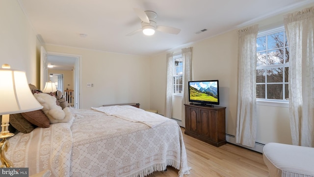 bedroom with light wood-type flooring, a baseboard heating unit, multiple windows, and visible vents