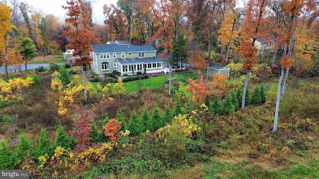 rear view of property featuring a forest view, an outdoor structure, and a lawn