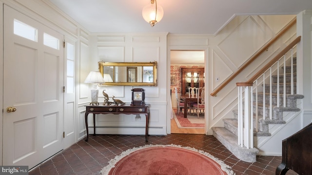 foyer entrance with a decorative wall, a baseboard heating unit, stairs, and dark tile patterned flooring