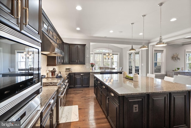 kitchen with a wealth of natural light, a kitchen island, an inviting chandelier, and under cabinet range hood