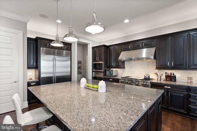 kitchen with built in appliances, a kitchen bar, dark wood-style floors, under cabinet range hood, and light stone counters
