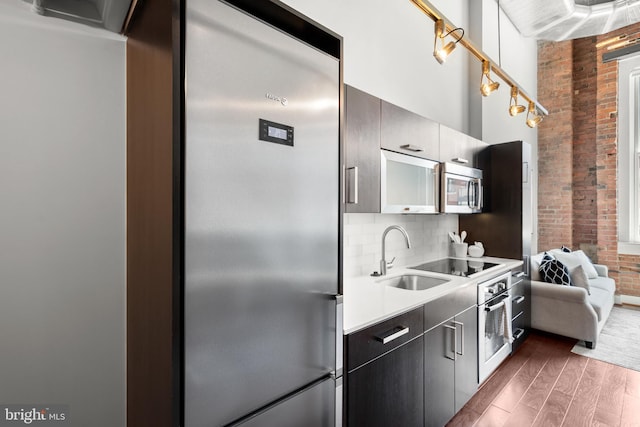 1401 R St NW Unit 304, Washington, DC 20009 - kitchen with decorative backsplash, dark wood-style flooring, brick wall, a sink, and stainless steel appliances