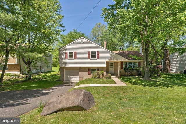 split level home with driveway, a chimney, a front yard, a garage, and brick siding