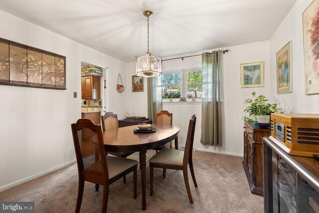 dining space with baseboards, light colored carpet, and a notable chandelier