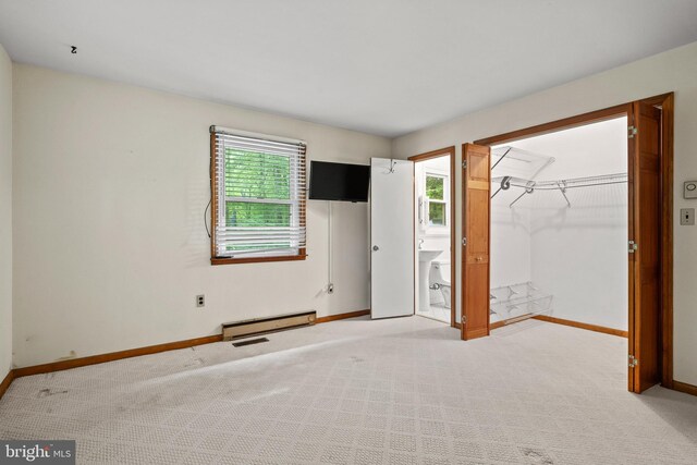 unfurnished bedroom featuring a walk in closet, light colored carpet, a sink, baseboards, and a baseboard radiator