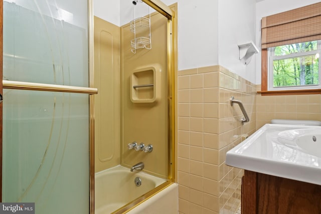 full bath with vanity, shower / bath combination with glass door, tile walls, and a wainscoted wall