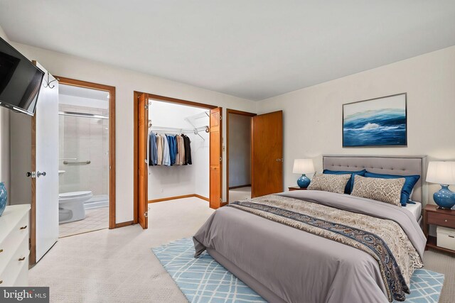 bedroom with a closet, baseboards, ensuite bathroom, a walk in closet, and light colored carpet