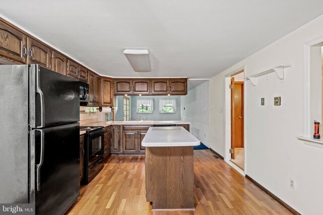 kitchen featuring a sink, light wood finished floors, light countertops, a center island, and black appliances