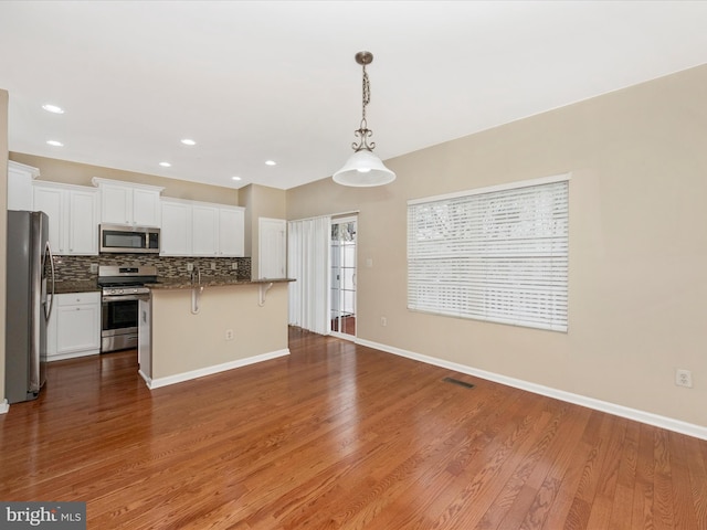 kitchen with visible vents, white cabinetry, wood finished floors, stainless steel appliances, and decorative backsplash