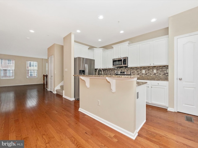 kitchen with a kitchen breakfast bar, light stone counters, a kitchen island with sink, visible vents, and stainless steel appliances