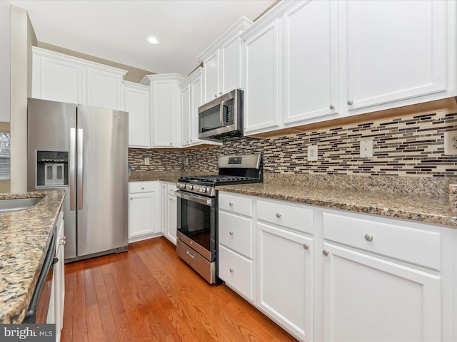 kitchen featuring light wood-type flooring, appliances with stainless steel finishes, decorative backsplash, and white cabinets