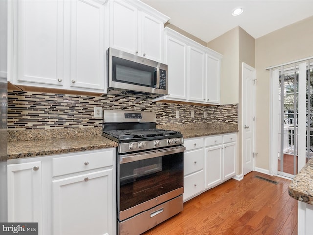 kitchen with stone counters, light wood-style flooring, white cabinetry, decorative backsplash, and appliances with stainless steel finishes