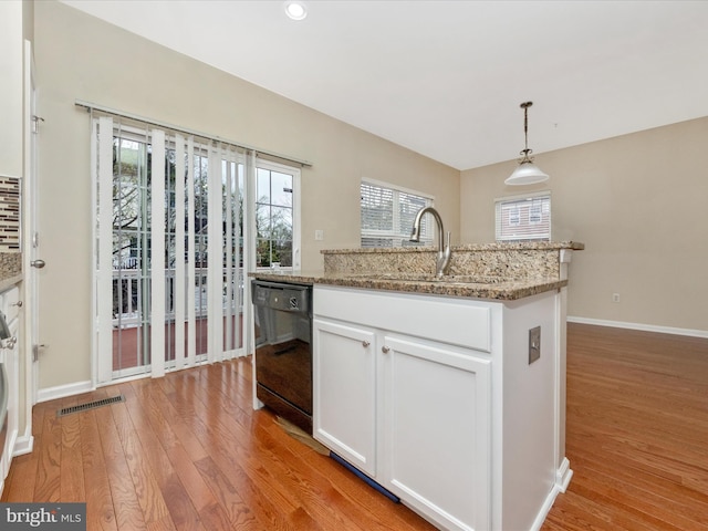 kitchen featuring light wood-type flooring, white cabinetry, decorative light fixtures, dishwasher, and a sink