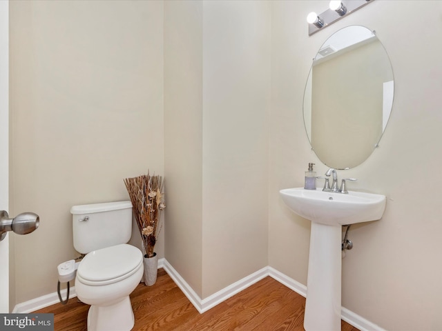 half bathroom with baseboards, toilet, and wood finished floors