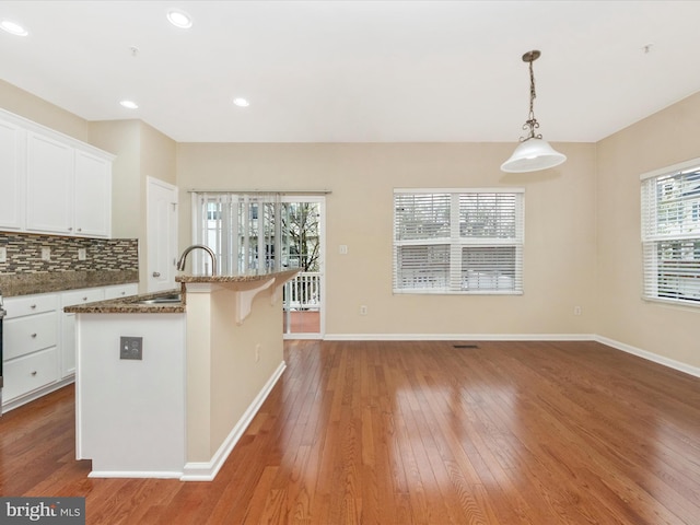 kitchen with a sink, white cabinetry, dark stone counters, backsplash, and hardwood / wood-style floors
