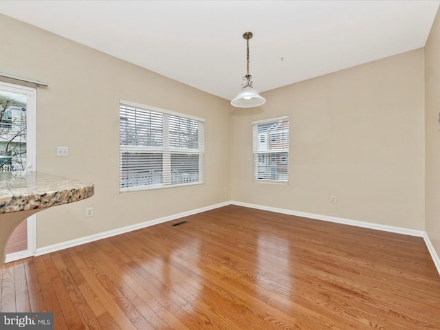 unfurnished dining area with a wealth of natural light, light wood finished floors, visible vents, and baseboards