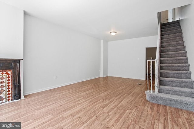 unfurnished living room featuring baseboards, light wood-type flooring, and stairs