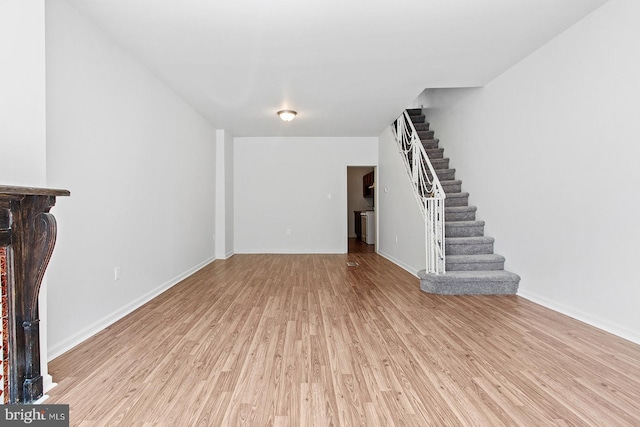 unfurnished living room featuring light wood finished floors, baseboards, and stairway