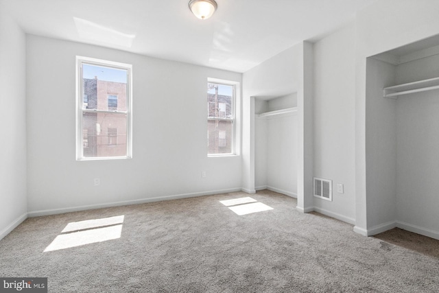 unfurnished bedroom featuring visible vents, multiple windows, two closets, and carpet floors