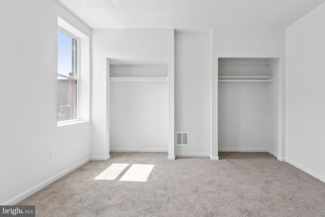 unfurnished bedroom featuring two closets, carpet flooring, baseboards, and visible vents