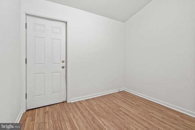 spare room with baseboards, light wood-style floors, and lofted ceiling