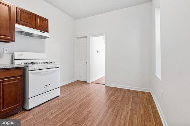 kitchen featuring white range with gas cooktop, light wood finished floors, baseboards, and under cabinet range hood