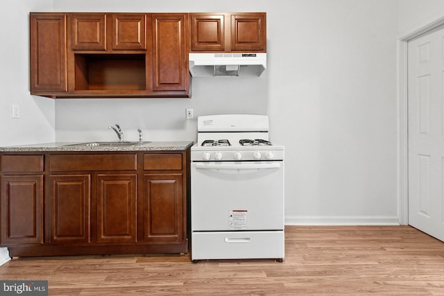 kitchen with a sink, light wood-type flooring, white gas range oven, and under cabinet range hood